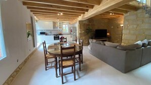 Amplia sala de estar con una mesa de comedor y sillas, una chimenea de piedra y una cocina moderna al fondo.
