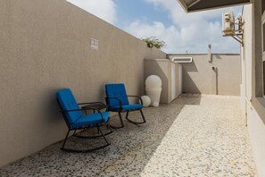 Une terrasse avec deux chaises bleues, un mur blanc et un sol carrelé.