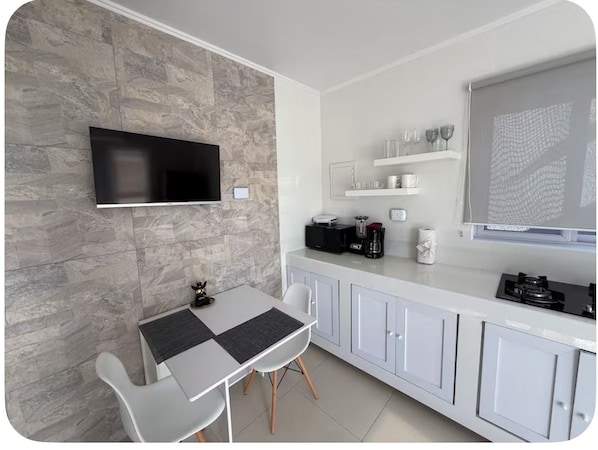Une cuisine moderne avec un mur en pierre, des armoires blanches, une table à manger avec des chaises et un téléviseur à écran plat fixé au-dessus du comptoir.