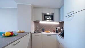 Een compacte keuken met een ingebouwde magnetron, een spoelbak en een aanrecht met een fruitschaal en een stokbrood.