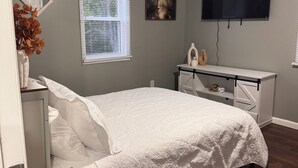 A bedroom with a bed, a desk, a television, and a ceiling fan.