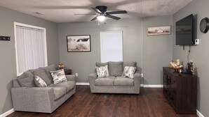 A living room with two grey sofas, a ceiling fan, a wooden cabinet, and a mounted TV.