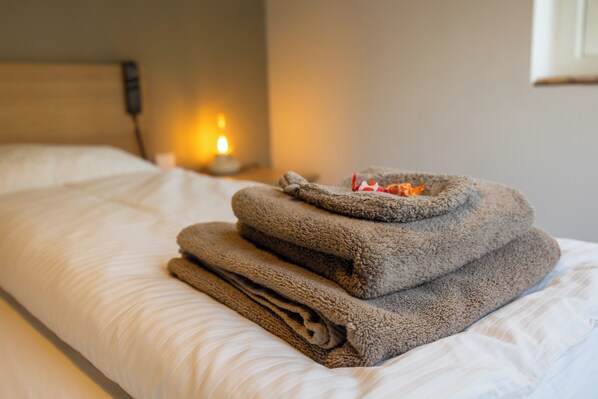 A neatly made bed with folded towels and a bedside lamp. - Sea Jewel - Very quiet location, near village and near the sea (Callantsoog)