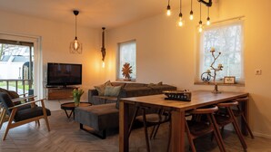 Una sala moderna con un sofá, un televisor, una mesa de comedor de madera y lámparas colgantes.