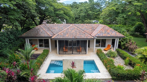 A house with a covered patio, a swimming pool, and lush garden landscaping.