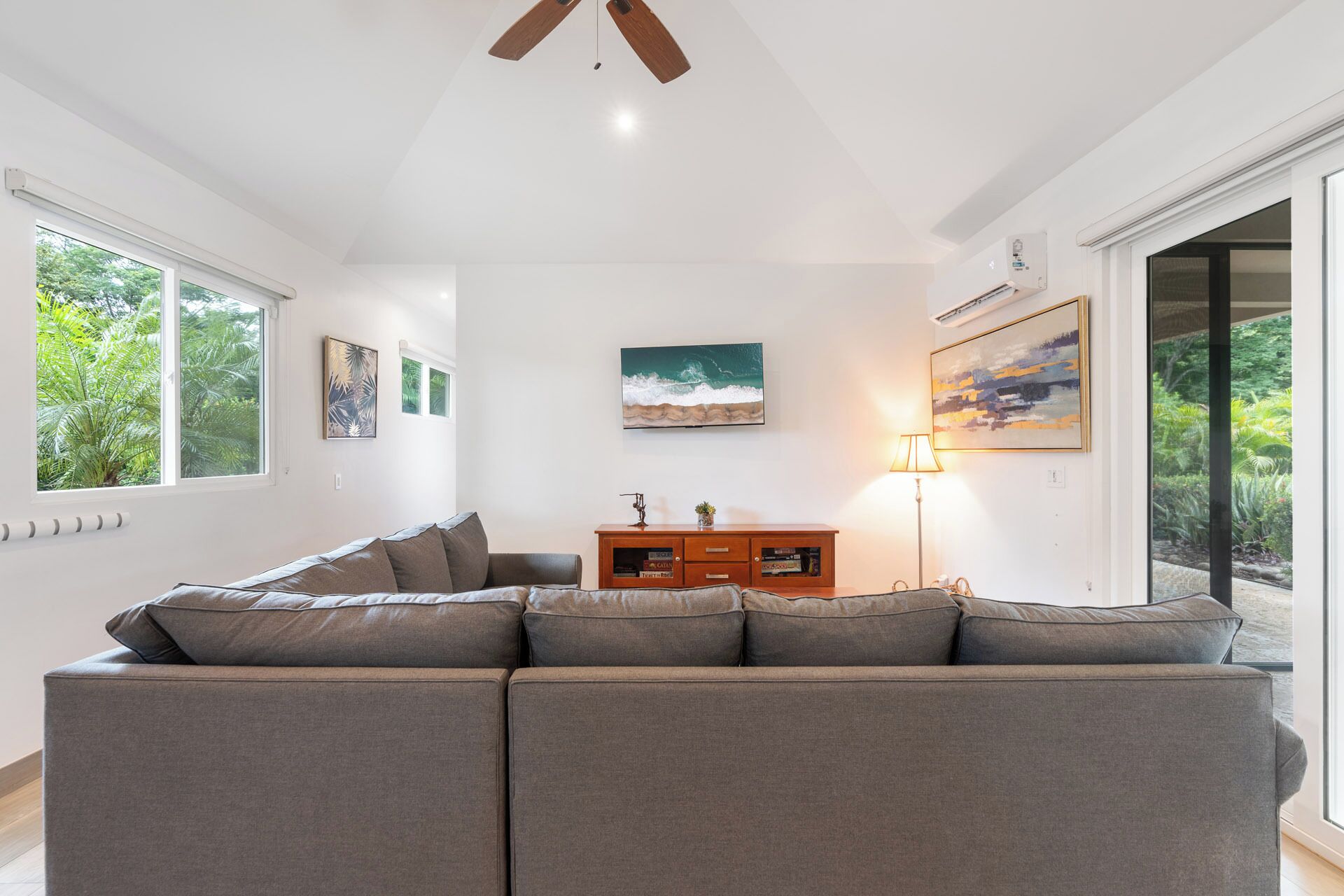 A modern living room with a grey sectional sofa, a wooden cabinet, and artwork on the walls.