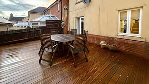 Une terrasse en bois avec une table ronde et des chaises, une antenne parabolique et une petite plante en pot.