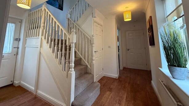 Un escalier avec des balustrades blanches et des marches recouvertes de moquette, menant à un palier. Deux suspensions lumineuses à motifs en zigzag sont suspendues au-dessus de l’escalier.