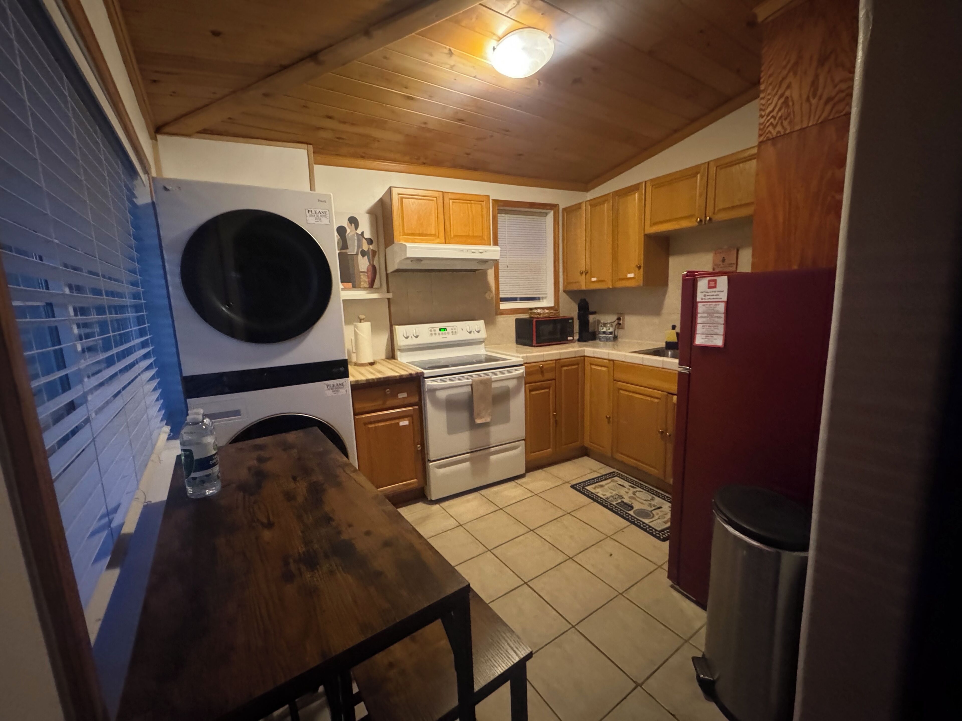 A compact kitchen with wooden cabinets, a washing machine, a stove, and a refrigerator.