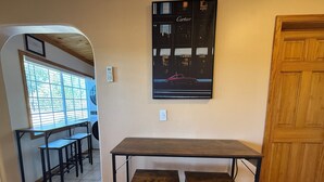 A room with a large wooden table and two stools, a window with blinds, a door, and a poster on the wall. - Charming 2-bedroom Guest house in Santa Fe with AC (Santa Fe)