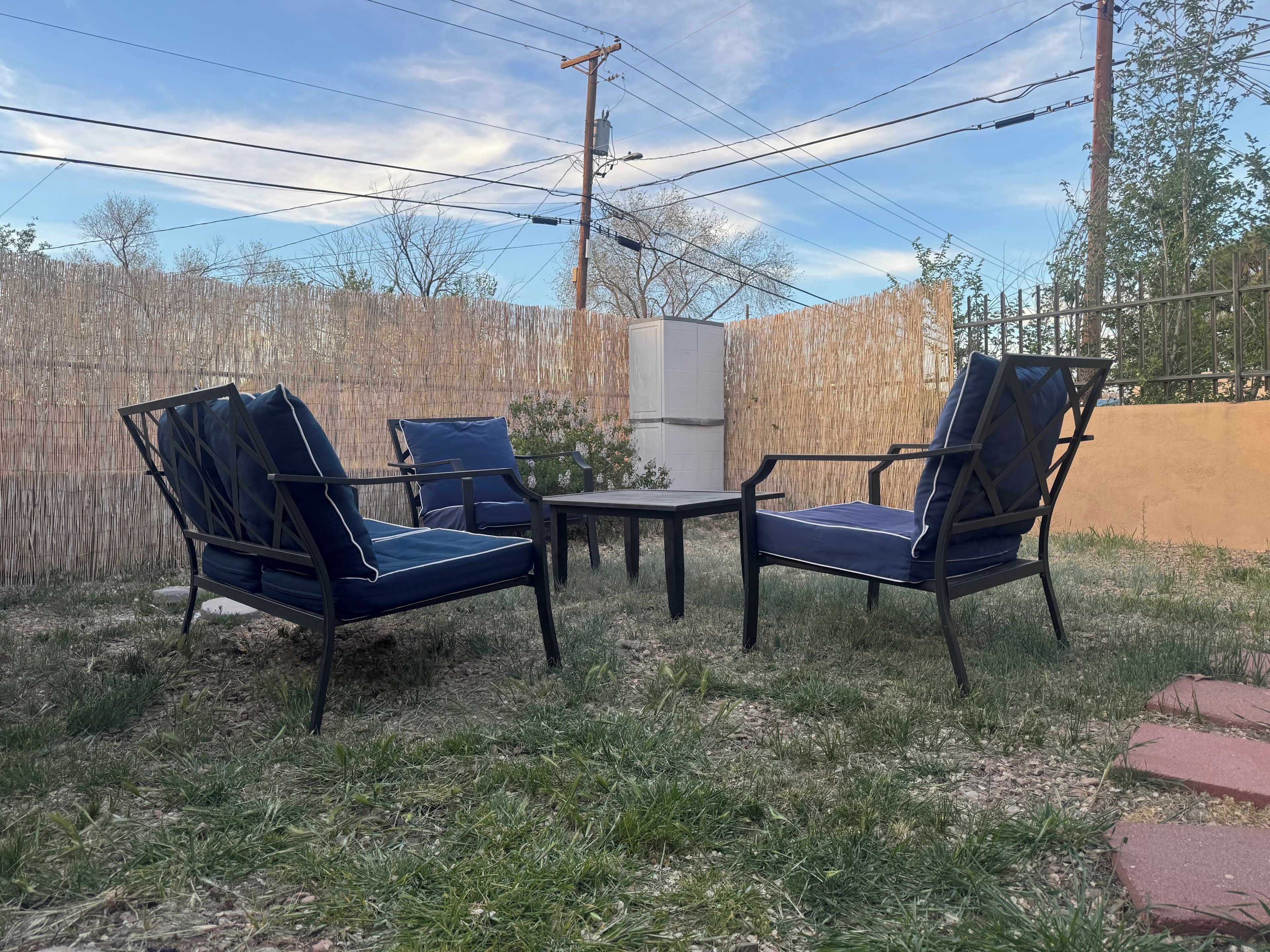 An outdoor seating area with two chairs and a table, surrounded by a wooden fence and power lines.