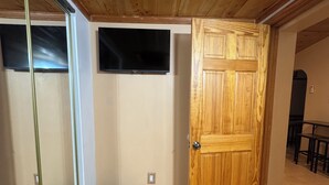 A room with a wooden ceiling, a wooden door, a television mounted on the wall, and two baskets on the floor. - Charming 2-bedroom Guest house in Santa Fe with AC (Santa Fe)