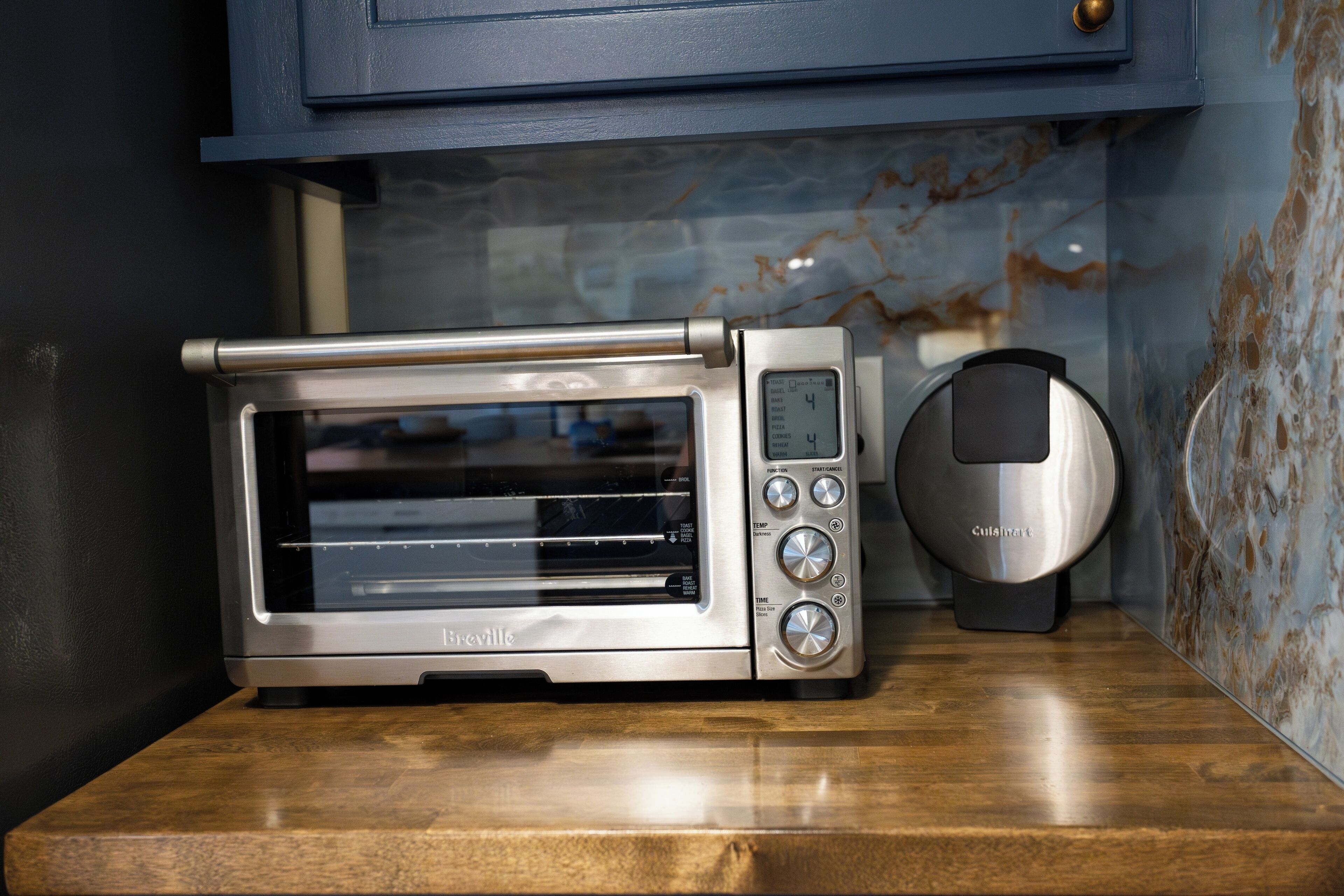 Um forno tostador Breville sobre uma bancada de madeira, com um armário azul acima.