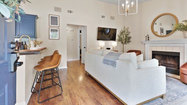 A modern living room with a sofa, a coffee table, and a fireplace. There is a kitchen area with a sink and cabinets. - New Meets Nostalgic- Cottage Sleeps 8 (Savannah)