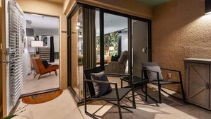 Ein modernes Wohnzimmer mit Glastür zum Balkon, einem Essbereich mit Tisch und Stühlen, und einer durch die Glastür sichtbaren Küche.
