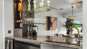 Eine moderne Küche mit Granit Arbeitsplatten, Edelstahlgeräten und einem Glastischchen, auf dem Weingläser präsentiert werden.