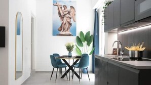 Una cocina moderna con armarios oscuros, un lavamanos de acero inoxidable y una zona de comedor con sillas azules y una mesa blanca.