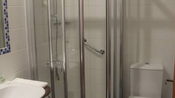 Un baño con ducha de vidrio, lavamanos blanco y retrete.