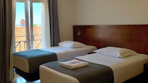 A hotel room with two beds, a wooden headboard, a large window with curtains, and a view of a building outside. - Hotel Vila Verde (Castro Verde)