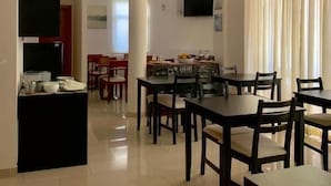 A spacious dining area with multiple tables and chairs, a kitchen area with a dining table and chairs, and a TV mounted on the wall. - Hotel Vila Verde (Castro Verde)