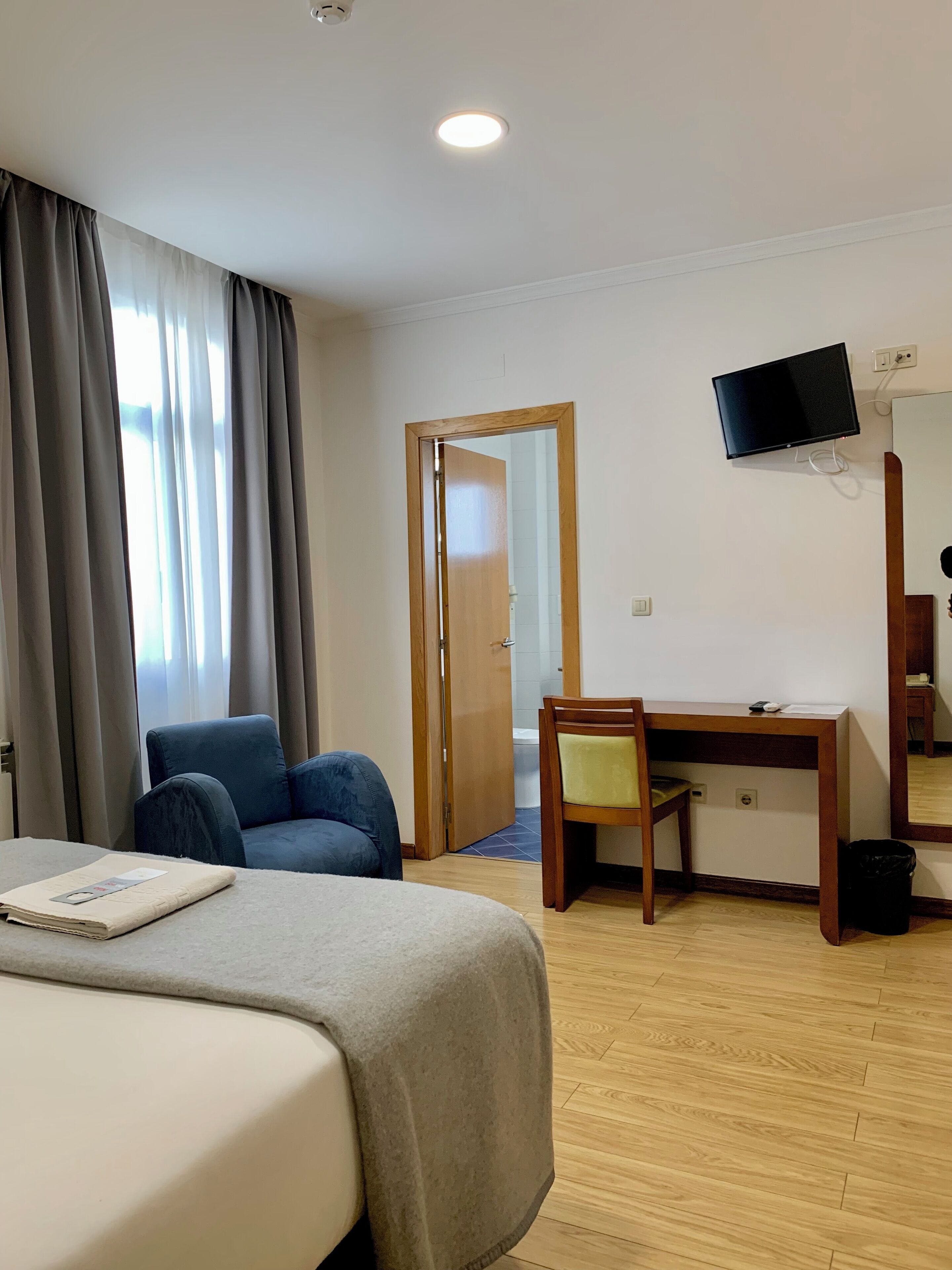 Habitación de hotel con una cama, un escritorio, una silla, un televisor y una puerta que da a un baño.