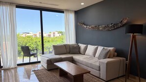 A modern living room with a sectional sofa, a wooden coffee table, and a large window with curtains.