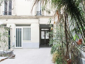 A building with a gated entrance, a covered outdoor seating area, and a potted plant in the foreground.