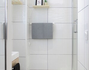 A bathroom with white tiled walls, a towel hanging on a rack, and a shelf with a plant.
