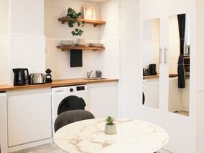 A compact kitchen with a built-in washing machine, a coffee maker, and a small potted plant on the countertop.