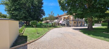Uma estrada de cascalho leva a uma área residencial com casas, um corredor coberto e uma grande árvore.