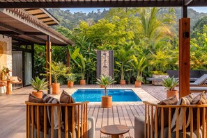 A poolside area with wooden deck seating, a pool, and lush tropical vegetation.