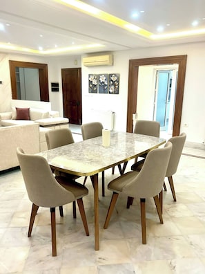 A dining area with a marble table and six chairs, a sofa in the background, and a door leading to another room. - Luxury Stay With Panoramic Sea Views, Tourist Zone (Sousse)