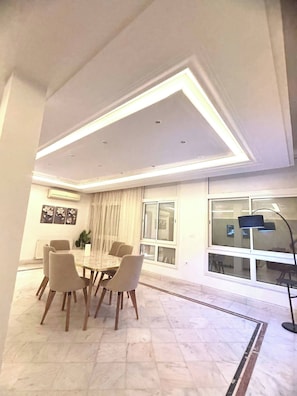 A dining area with a round table, six chairs, and a modern ceiling light fixture. - Luxury Stay With Panoramic Sea Views, Tourist Zone (Sousse)