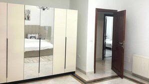 Ein Schlafzimmer mit großem Kleiderschrank, einem Bett, einer Deckenleuchte und einer Tür zu einem anderen Raum.