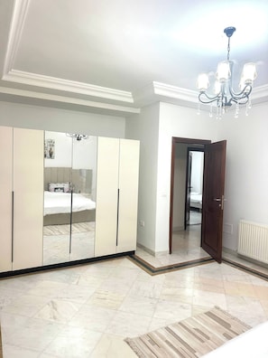 Une chambre dotée d’une grande armoire, d’un lit, d’un lustre et d’une porte donnant sur une autre pièce.
