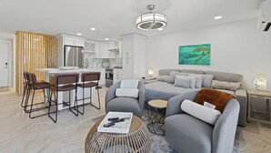 A modern living room with a grey sofa, a coffee table, and a dining area with chairs and a kitchen in the background.