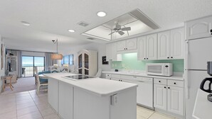 A modern kitchen with white cabinetry, a central island, a microwave, and a ceiling fan.