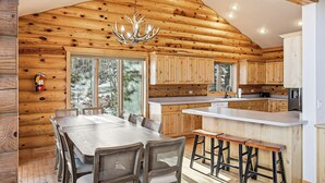A log cabin interior with a dining area, kitchen, and large windows. - Ridgeview Retreat, 5-bedroom cabin in Brian Head with jacuzzi, views and stocked (Brian Head)