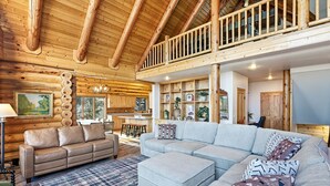A spacious living area with a large sofa, a smaller sofa, and a dining table. There is a kitchen area with wooden cabinets and a balcony with a wooden railing. - Ridgeview Retreat, 5-bedroom cabin in Brian Head with jacuzzi, views and stocked (Brian Head)