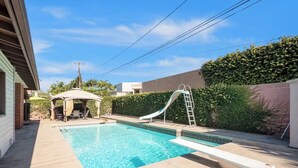 Un patio trasero con piscina, tobogán y una zona de estar cubierta.