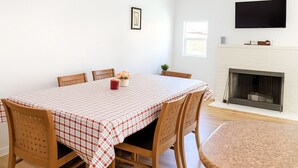 Un comedor con mantel a cuadros, sillas de madera, chimenea y televisor de pantalla plana montado en la pared.