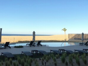 A poolside area with lounge chairs and umbrellas, a palm tree, and a view of the beach. - Charming 2-bedroom resort with fitness room and AC in sunny Cabo San Lucas (Cabo San Lucas)