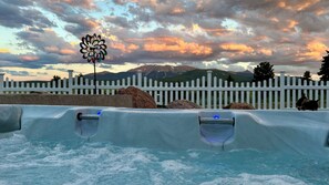 A hot tub with a view of mountains and a white picket fence in the background.