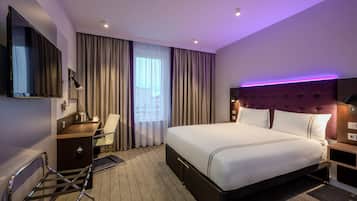 A hotel room with a bed, a desk, a chair, a TV, and a window with curtains.