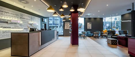 Un vestíbulo moderno de hotel con mostrador de recepción, zona de estar y ventanas amplias.