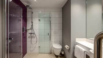 Un baño moderno con ducha envuelta en vidrio, inodoro blanco y lavamanos con espejo.
