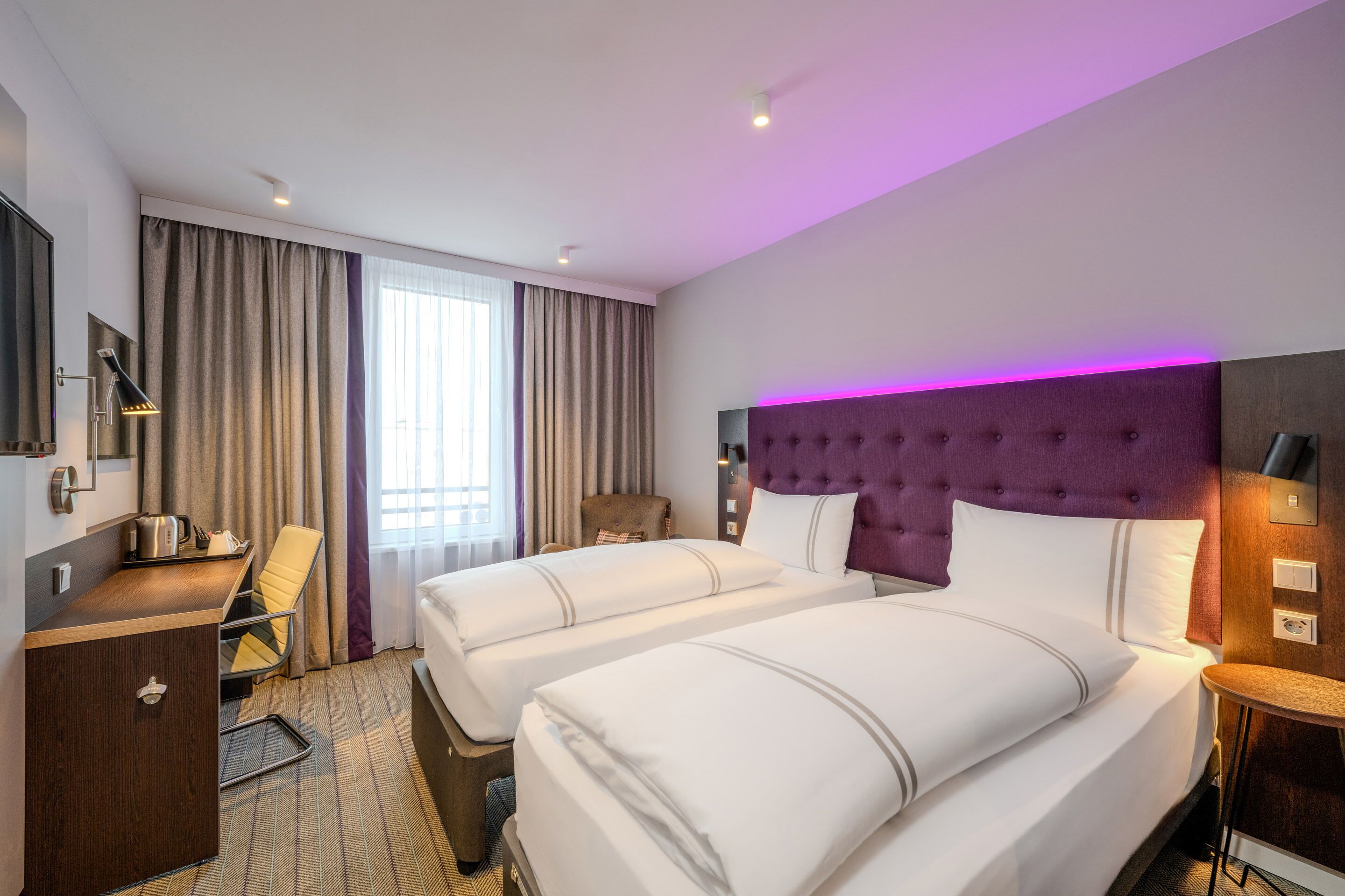 A hotel room with two beds, a desk, a chair, and a small table.