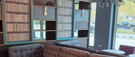 Un área de estar moderna con un sofá modular, mesas redondas y estanterías llenas de libros.
