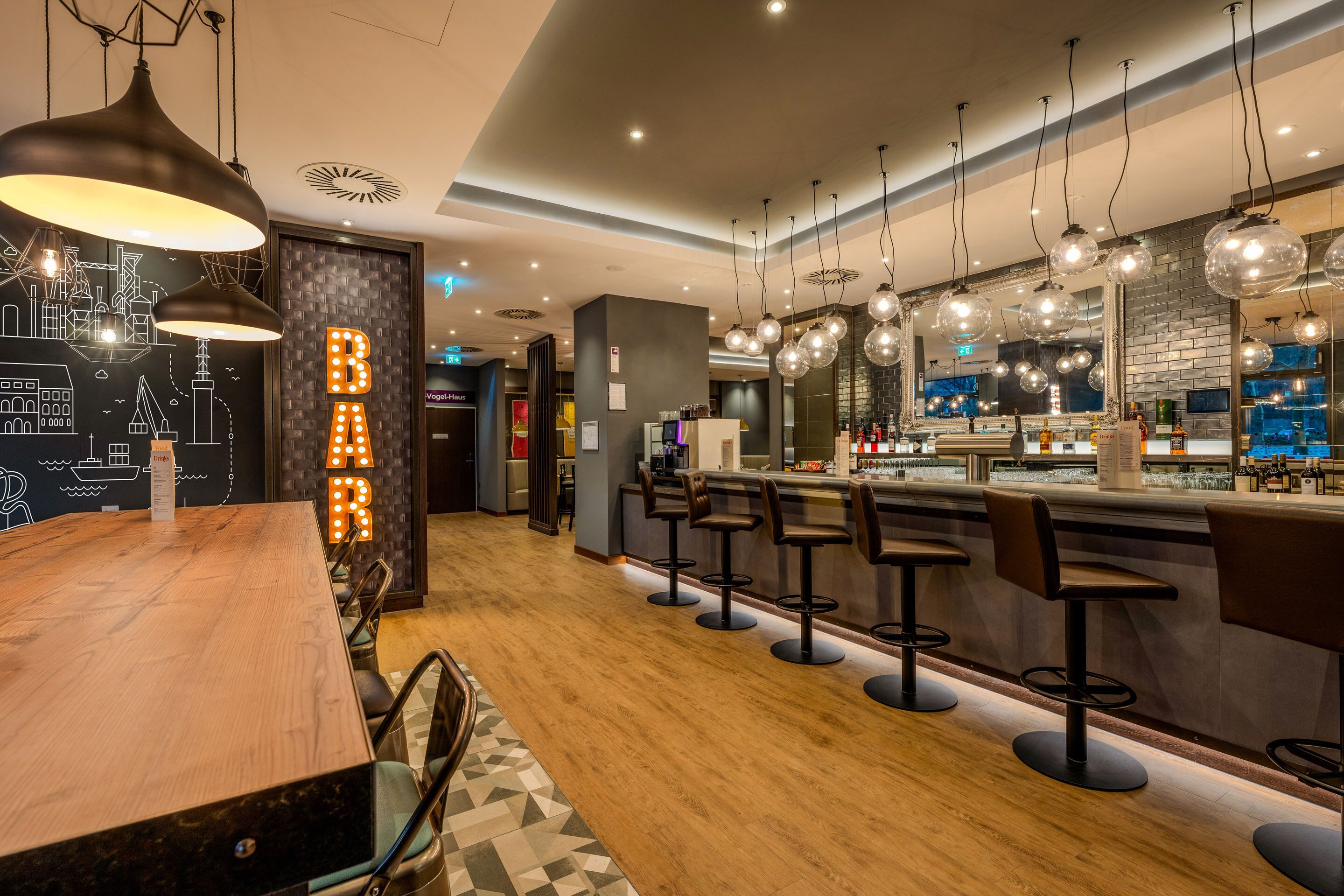Un espace bar moderne avec un plancher en bois, des tabourets de bar, des luminaires suspendus et une fresque représentant un paysage urbain.
