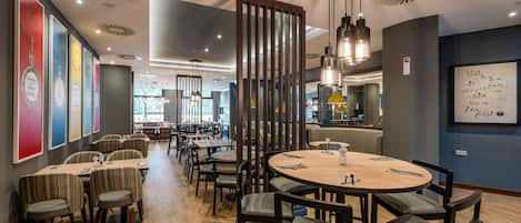 A modern dining area with tables and chairs, a large window, and a decorative wall.